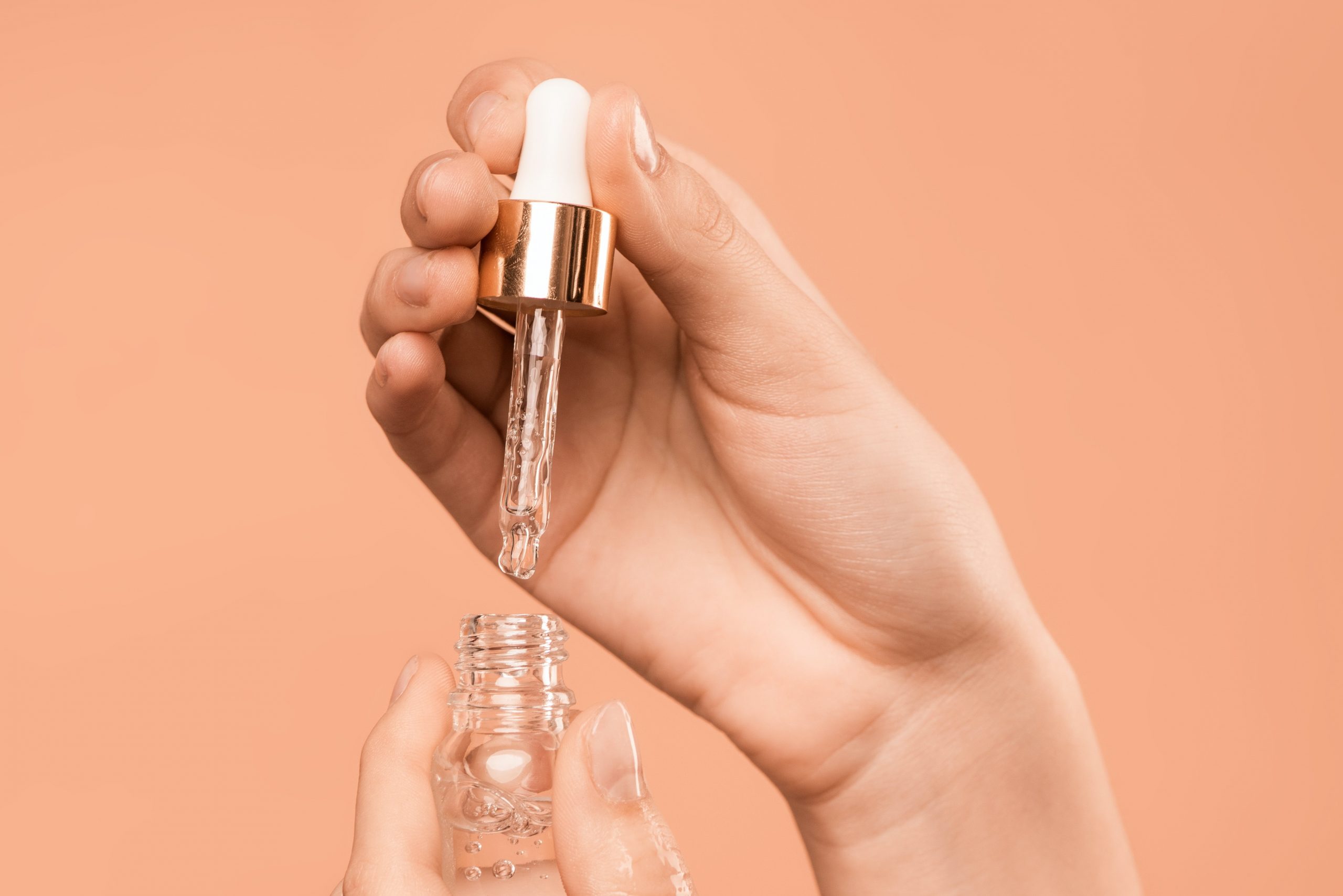 hands holding small serum bottle with peach backdrop