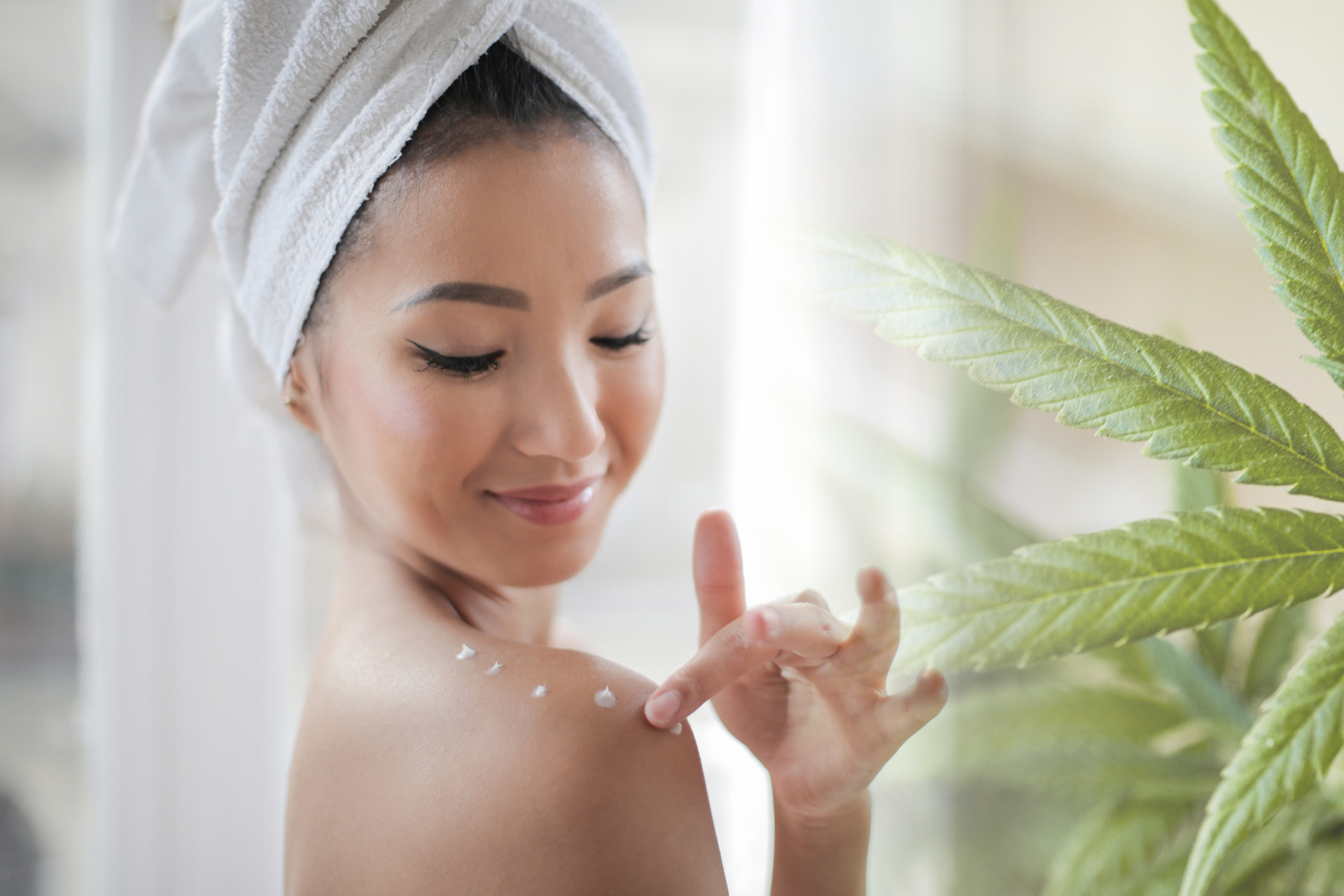 woman with towel on head putting on lotion on shoulders